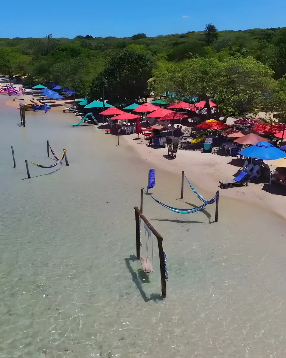 Barracas com guarda-sóis coloridos e redes armadas na água rasa da Lagoa do Carcará
