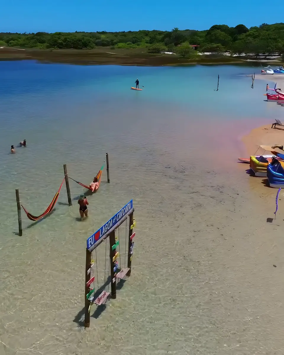 Redes coloridas dentro da água rasa e a placa Eu amo Lagoa do Carcará